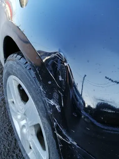 Aripă neagră cu zgârieturi în vopsea, deasupra roții din față